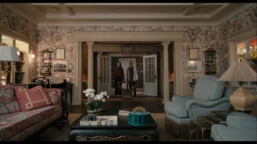 Frame from the show Only Murders in the Building with two people standing in a lushly decorated apartment light floral wallpaper.
