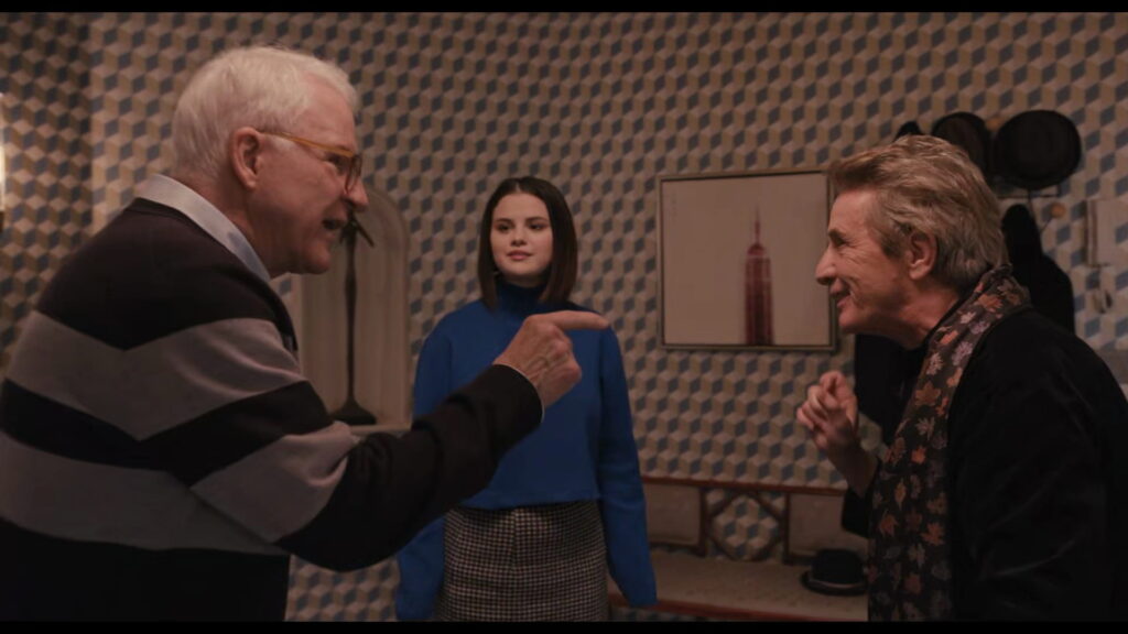 Frame from the show Only Murders in the Building with three people talking in front of a geometric wallpaper pattern.