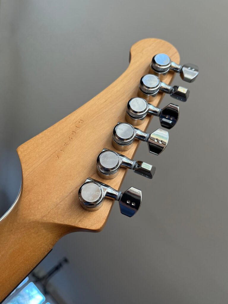Back of electric guitar headstock with light wood finish and locking silver tuners