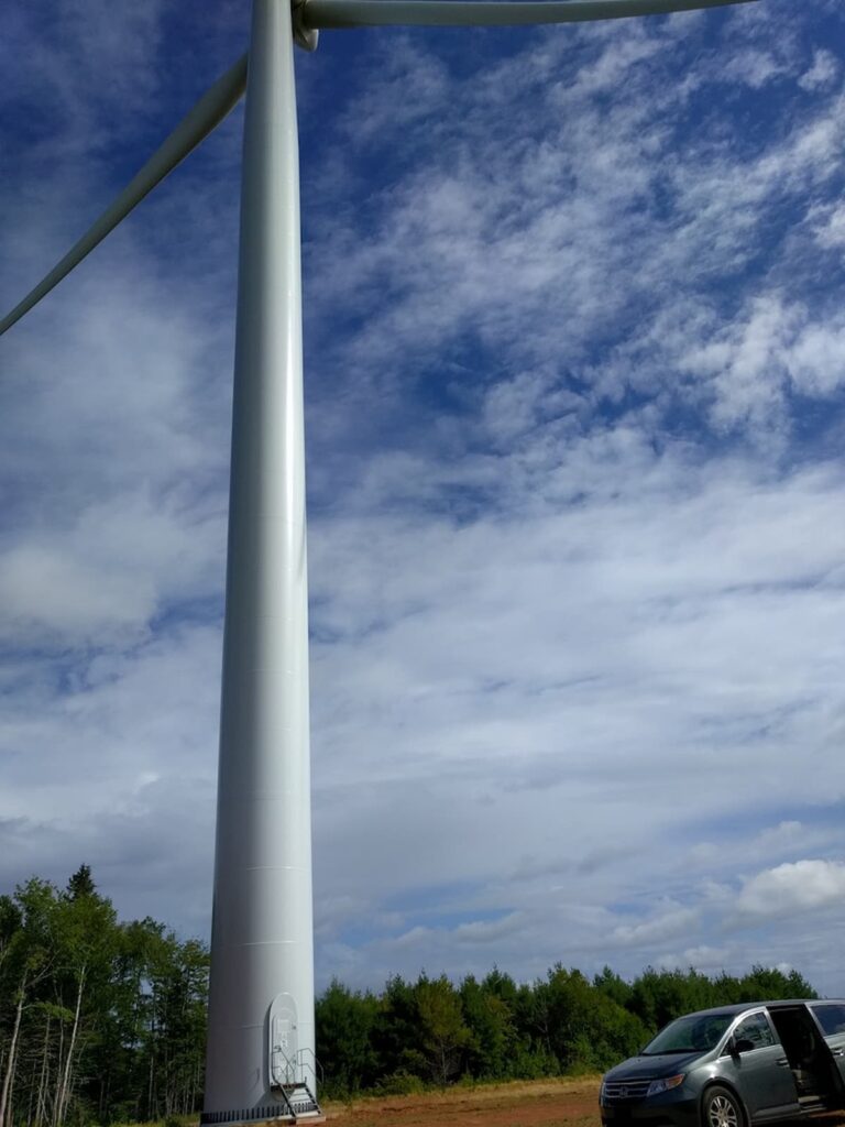 Photo of a large wind turbine with a minivan parked near the base.