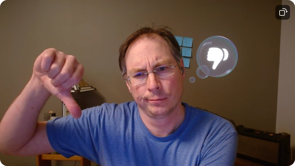Screenshot of webcam showing a tired dad in a blue t-shirt making a thumbs-down gesture and grumpy face and an overlay of a cartoonish 3d bubble graphic with a thumbs-down icon in it.