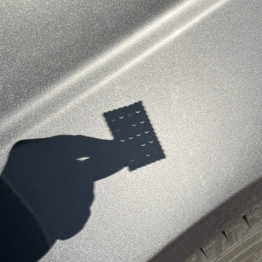 Shadow of a hand holding a rectangular cracker with small holes in the shape of a partial eclipse.